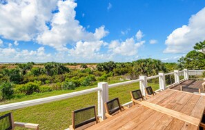 A wooden deck with outdoor seating, surrounded by lush greenery and a clear blue sky. - Oceanfront - Resort Access + Golf Cart (Fripp Island)