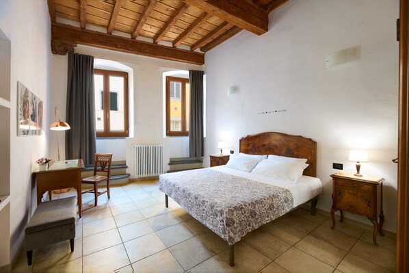 A bedroom with a large bed, a wooden headboard, a desk with a chair, and a radiator. - San Niccolò Luxury Apartment (Firenze)