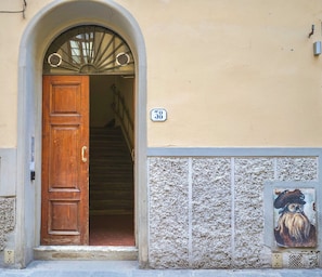 A building entrance with a wooden door, a number '38' sign, and a textured wall with a small painting. - San Niccolò Luxury Apartment (Firenze)