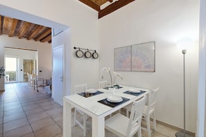A dining area with a white table set for four, a wall-mounted clock, and a framed artwork. - San Niccolò Luxury Apartment (Firenze)