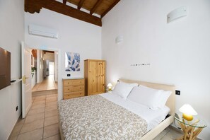 A bedroom with a bed, a wooden wardrobe, a bedside table with a lamp, and a wall with a decorative sign. - San Niccolò Luxury Apartment (Firenze)