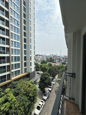Ein Hochhaus mit mehreren Etagen, einem Balkon und Blick auf eine Straße mit parkenden Autos und Bäumen.
