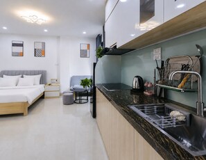 Eine moderne Küche mit integrierter Kochinsel, ein Essbereich mit grauem Sofa und ein Schlafzimmer mit Bett und Nachttischen.