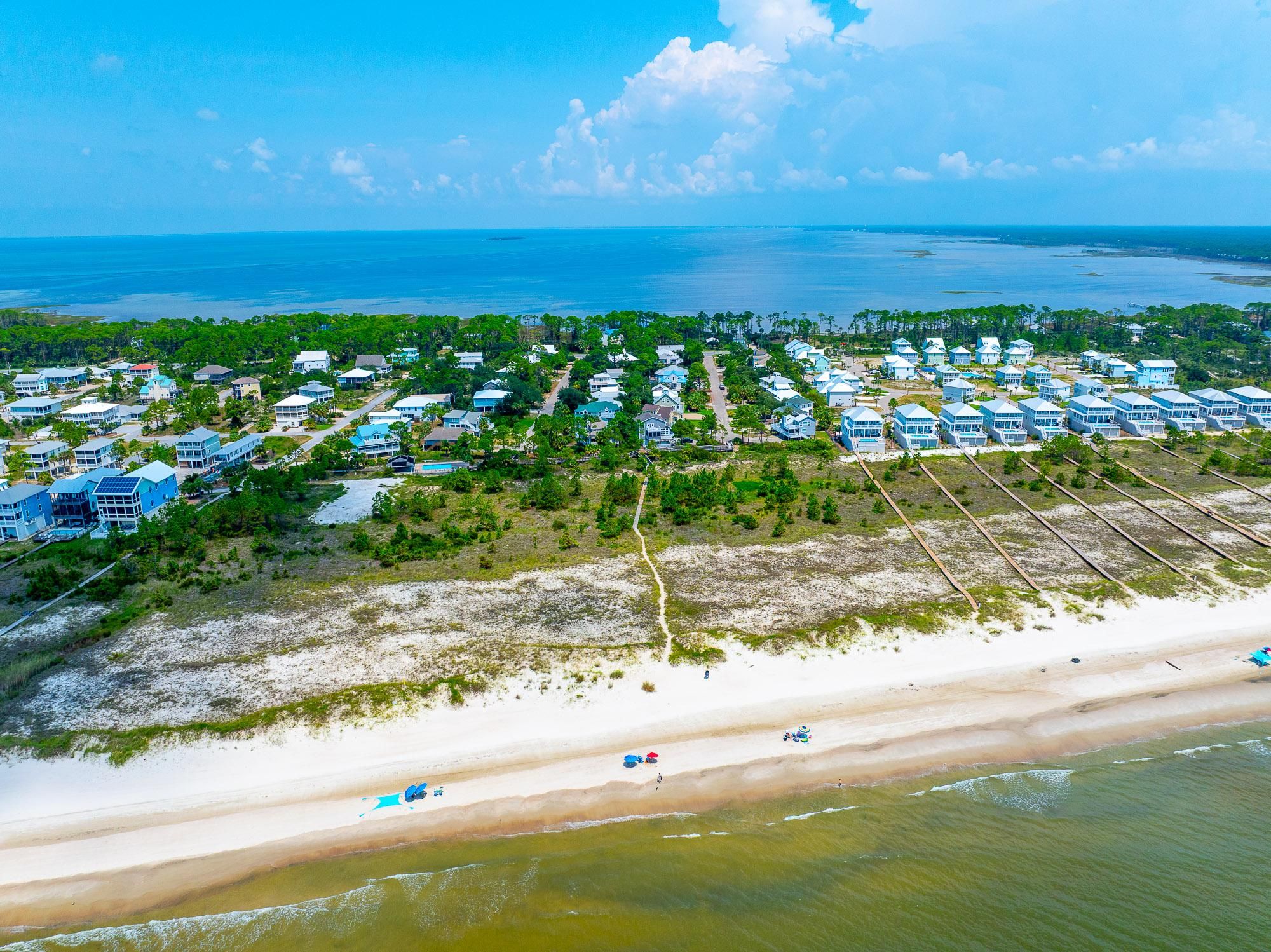An aerial view of a coastal residential area with houses, a beach, and a clear sky.