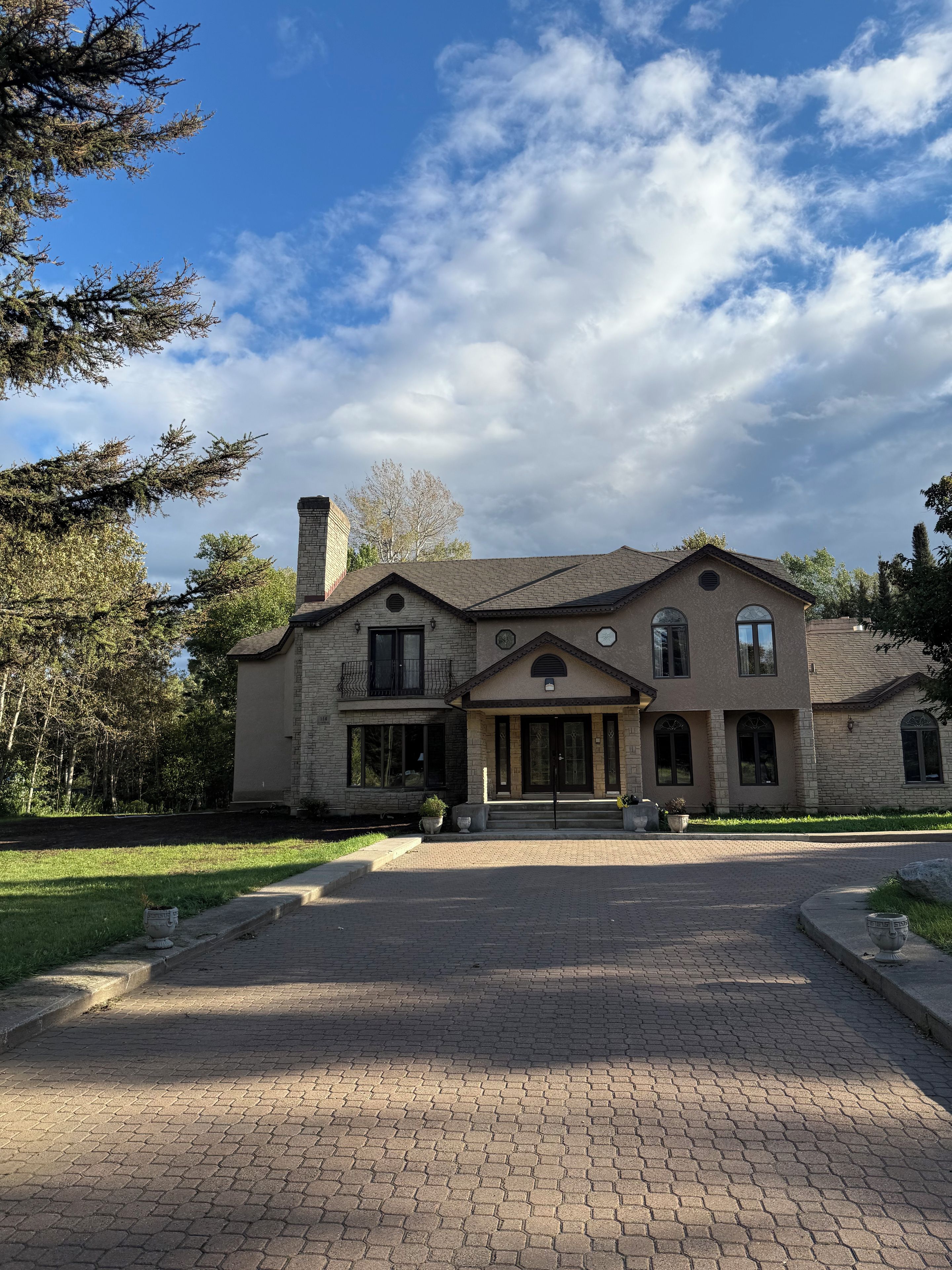 A two-story house with a stone facade, a front porch, and a driveway leading to the entrance.