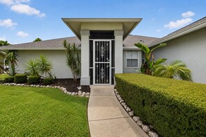 A residential house with a gated entrance, a well-maintained lawn, and a variety of tropical plants. - Imperial Retreat | Family Friendly Pool Home (Bonita Springs)