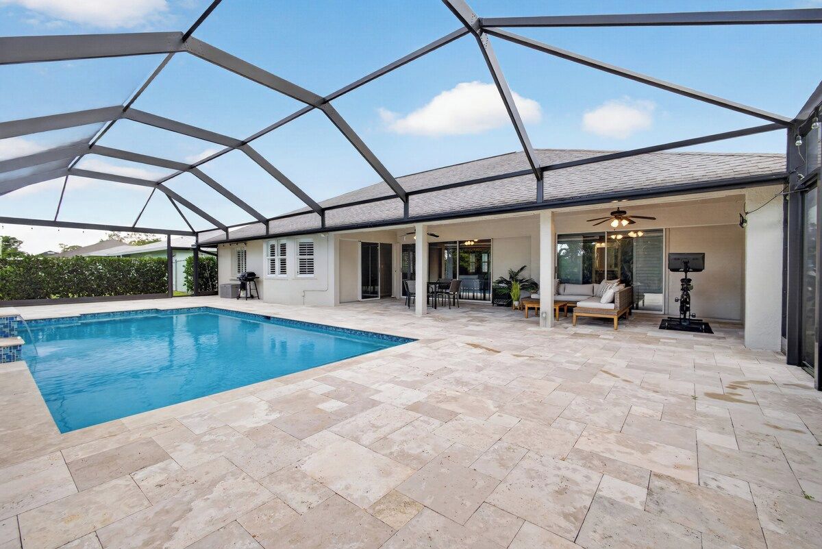 A covered outdoor swimming pool with a patio area, seating, and a ceiling fan.