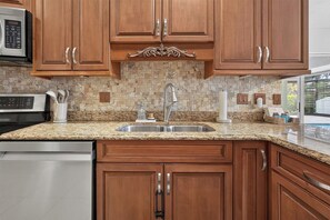A kitchen with wooden cabinets, a granite countertop, a stainless steel sink, and a built-in microwave. - Imperial Retreat | Family Friendly Pool Home (Bonita Springs)