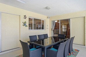 A glass-top dining table with wicker chairs, a sliding glass door, and a ceiling light fixture. - Piece of Paradise | 3BR Waterfront Pool Retreat (Cape Coral)