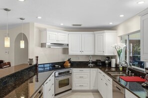 A modern kitchen with white cabinetry, a granite countertop, stainless steel appliances, and recessed ceiling lighting. - Piece of Paradise | 3BR Waterfront Pool Retreat (Cape Coral)