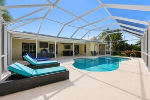 A covered outdoor swimming pool with lounge chairs and a sunshade structure. - Piece of Paradise | 3BR Waterfront Pool Retreat (Cape Coral)
