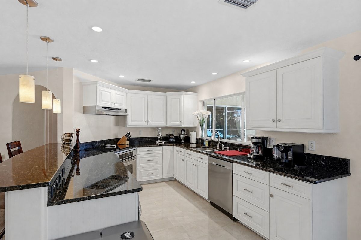 A modern kitchen with white cabinetry, a granite countertop, and stainless steel appliances.