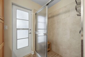A bathroom with a glass shower door, a white door with frosted glass panels, and beige tiled walls. - Piece of Paradise | 3BR Waterfront Pool Retreat (Cape Coral)