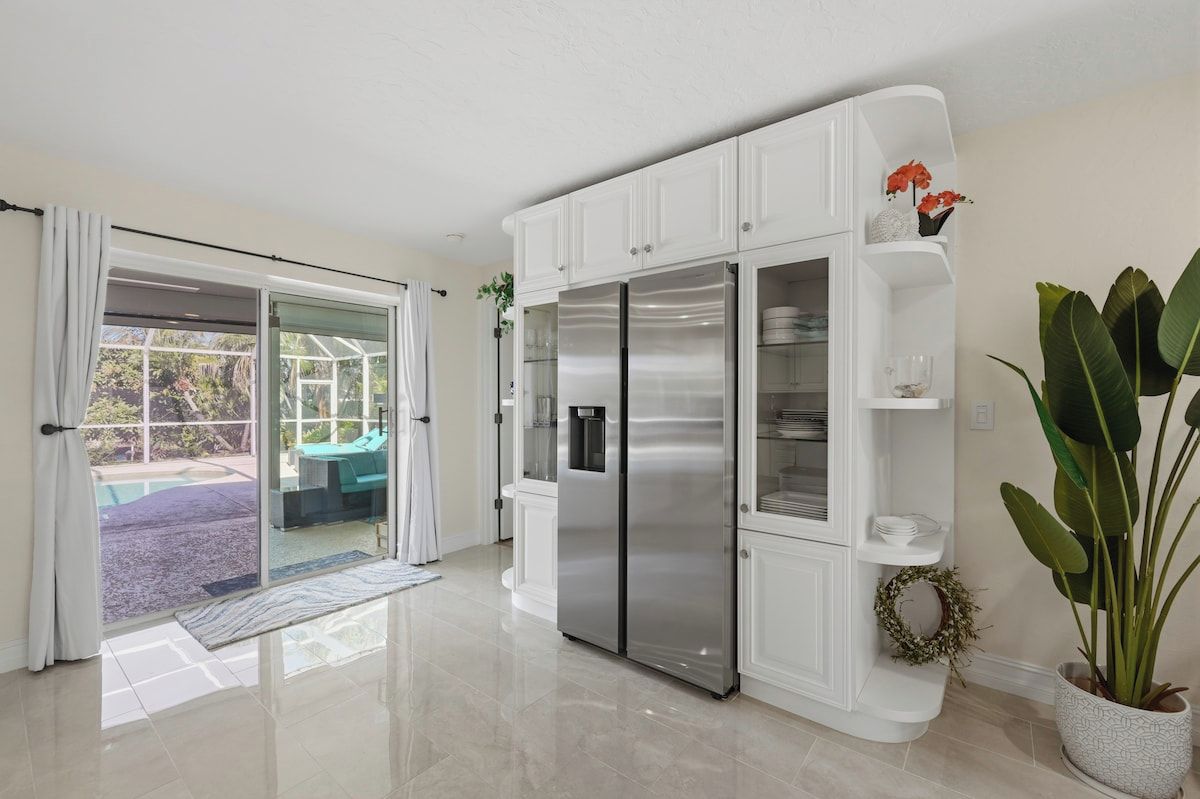 A modern kitchen with white cabinetry, a stainless steel refrigerator, and a potted plant.