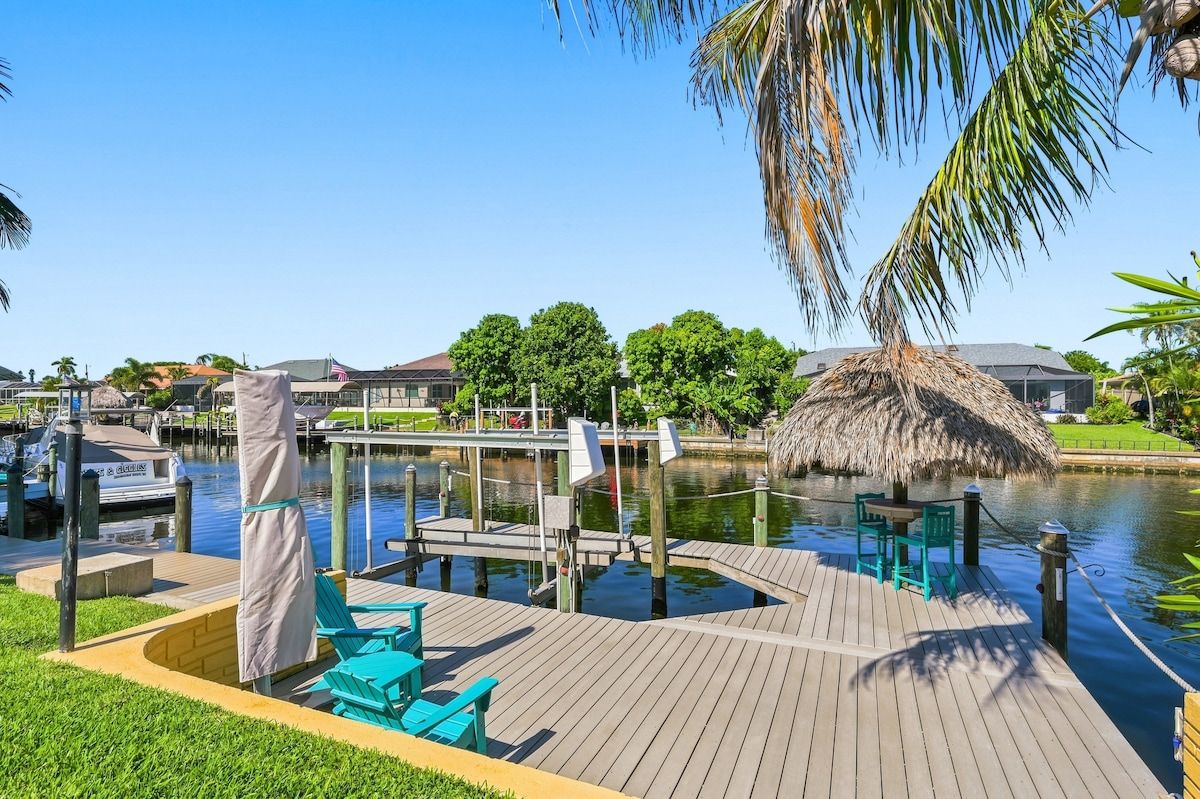 A waterfront dock with chairs and a table, a thatched-roof structure, and a clear view of the water.