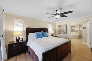 A bedroom with a bed, nightstands, a ceiling fan, and a door leading to another room. - Piece of Paradise | 3BR Waterfront Pool Retreat (Cape Coral)