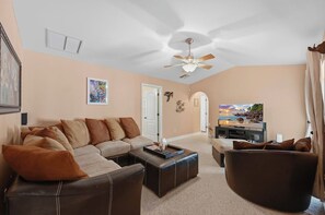 A living room with a sofa, ottoman, and a television. - Piece of Paradise | 3BR Waterfront Pool Retreat (Cape Coral)