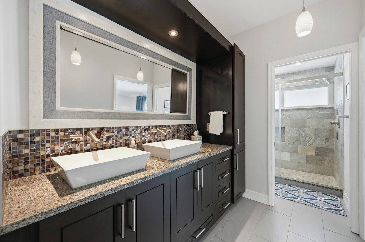A modern bathroom with two sinks, dark cabinetry, and a shower area.
