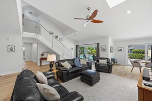 A spacious living room with a black leather sofa, a coffee table, and a ceiling fan. - The Palms at McGregor | Luxury 4BR Pool Home (Fort Myers)