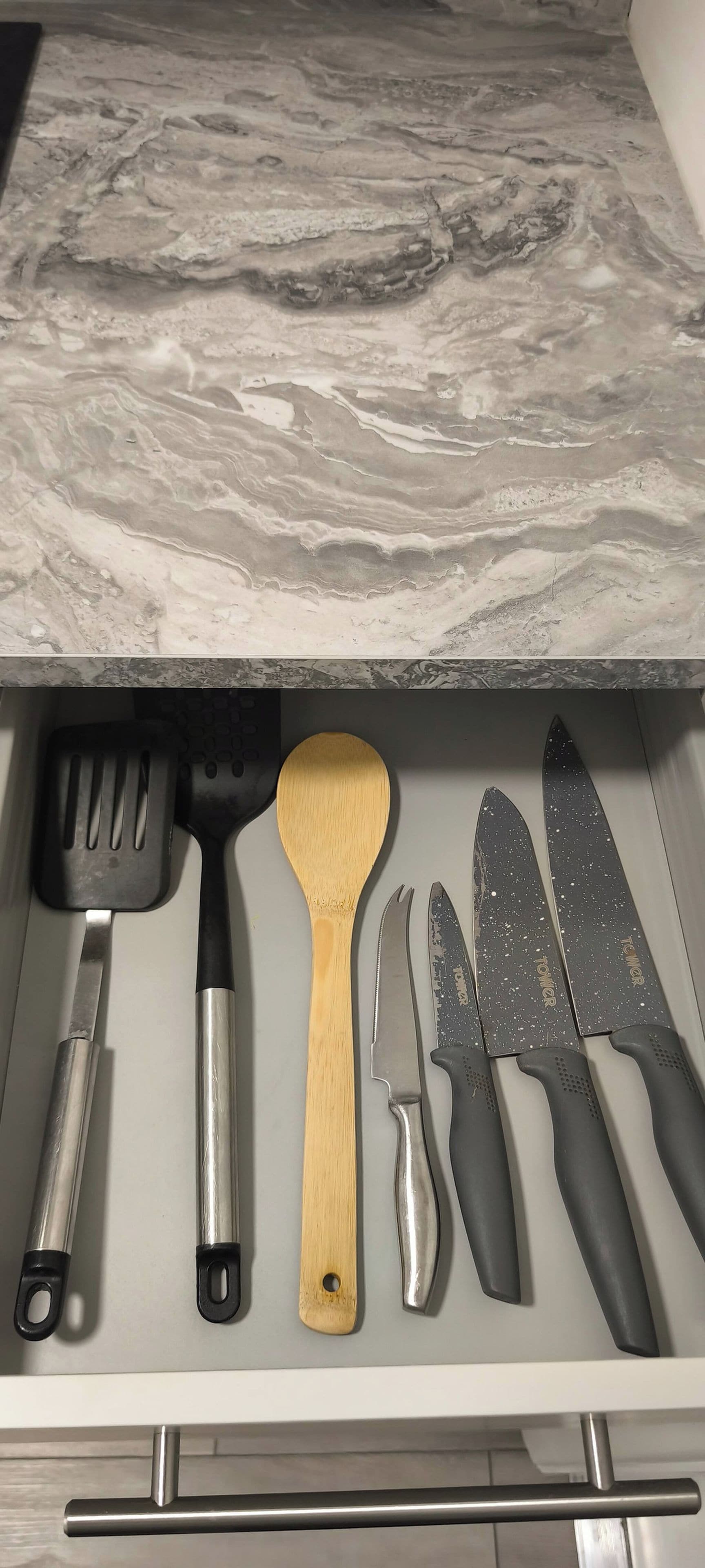 Un cajón con utensilios de cocina, incluyendo una espátula, cuchara de madera y cuchillos.