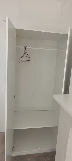 Ein weißer Kleiderschrank mit zwei Einlegeböden und einer Kleiderstange.