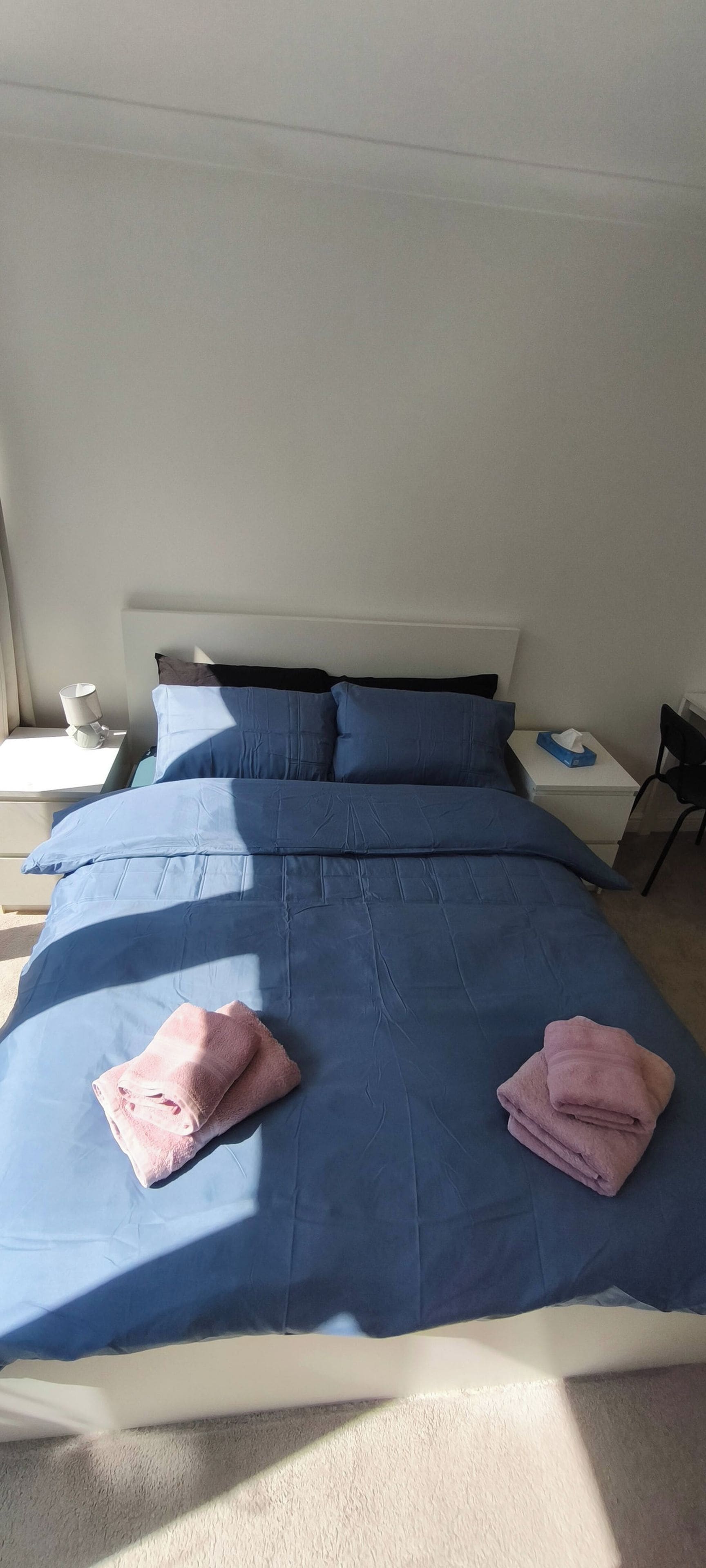 A hotel room with a bed, pillows, a nightstand, a lamp, and a chair.