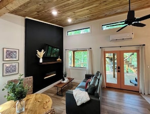 A modern living room with a sofa, a coffee table, and a fireplace. There are windows and a ceiling fan. - Tree Loft: Your romantic treetop escape near Hot Springs. (Bismarck)