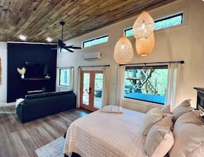 A bedroom with a bed, a ceiling fan, and a large window with a view of the outdoors. - Tree Loft: Your romantic treetop escape near Hot Springs. (Bismarck)