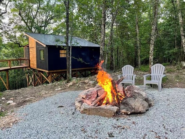 A cabin with a deck, a fire pit, and two chairs. - Tree Loft: Your romantic treetop escape near Hot Springs. (Bismarck)