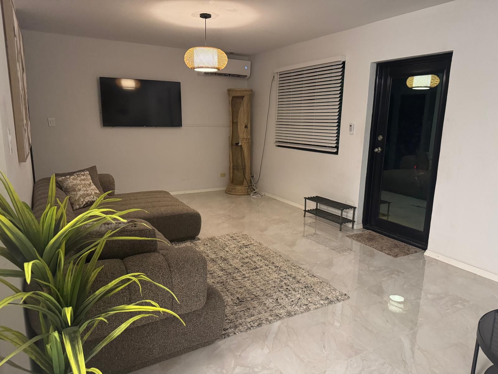 Un salon moderne avec un canapé, un téléviseur à écran plat, un luminaire décoratif et une porte-fenêtre coulissante.