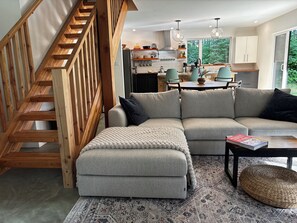Ein modernes Wohnzimmer mit einer Holztreppe, einem grauen Ecksofa, einem Couchtisch und einem gemusterten Teppich.