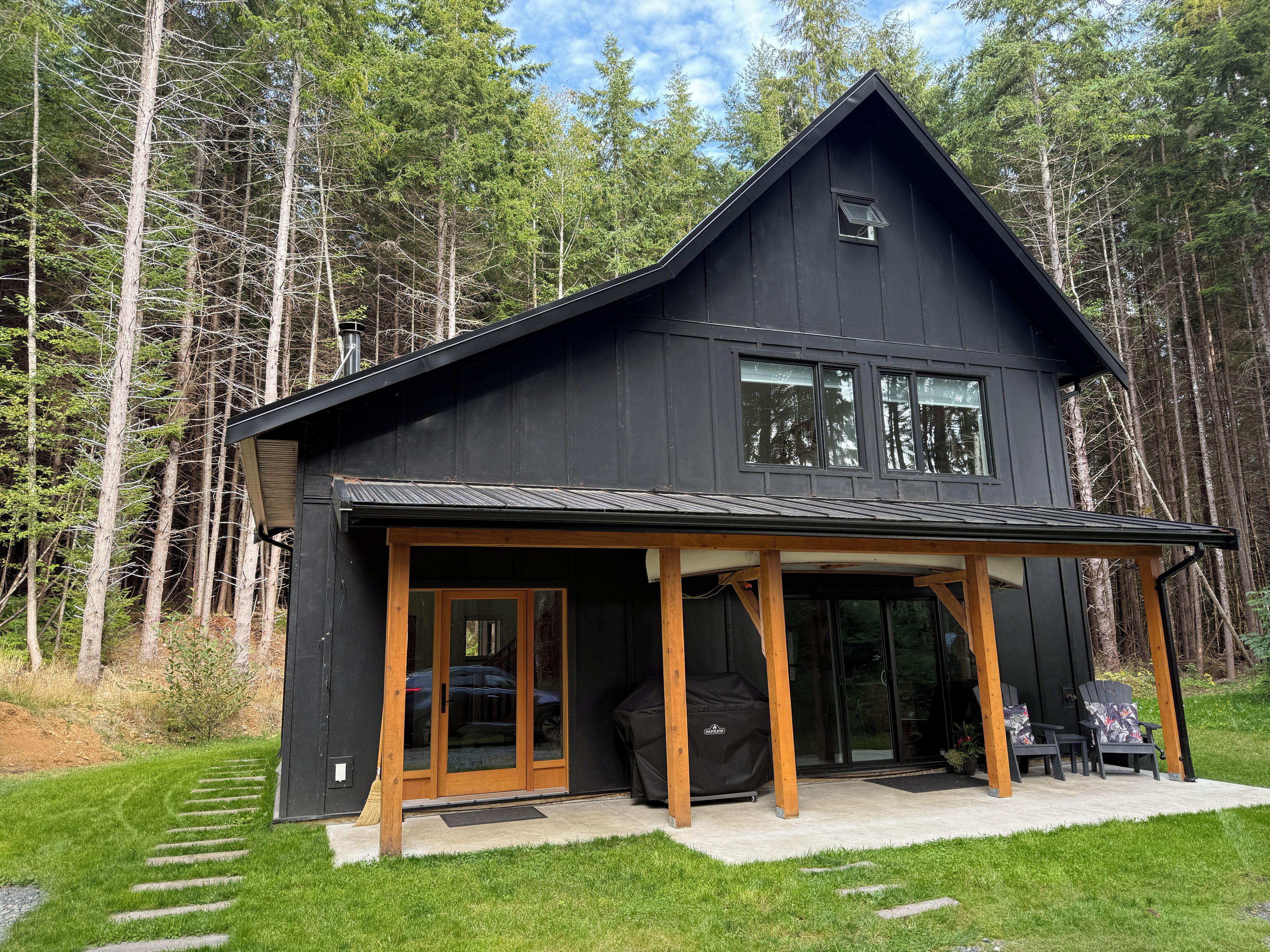 A modern two-story cabin with a covered porch and a carport.