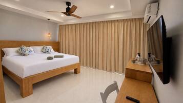Ein Hotelzimmer mit einem Bett, einem Schreibtisch, einem Sessel, einem Deckenventilator, einem Fernseher und Vorhängen.