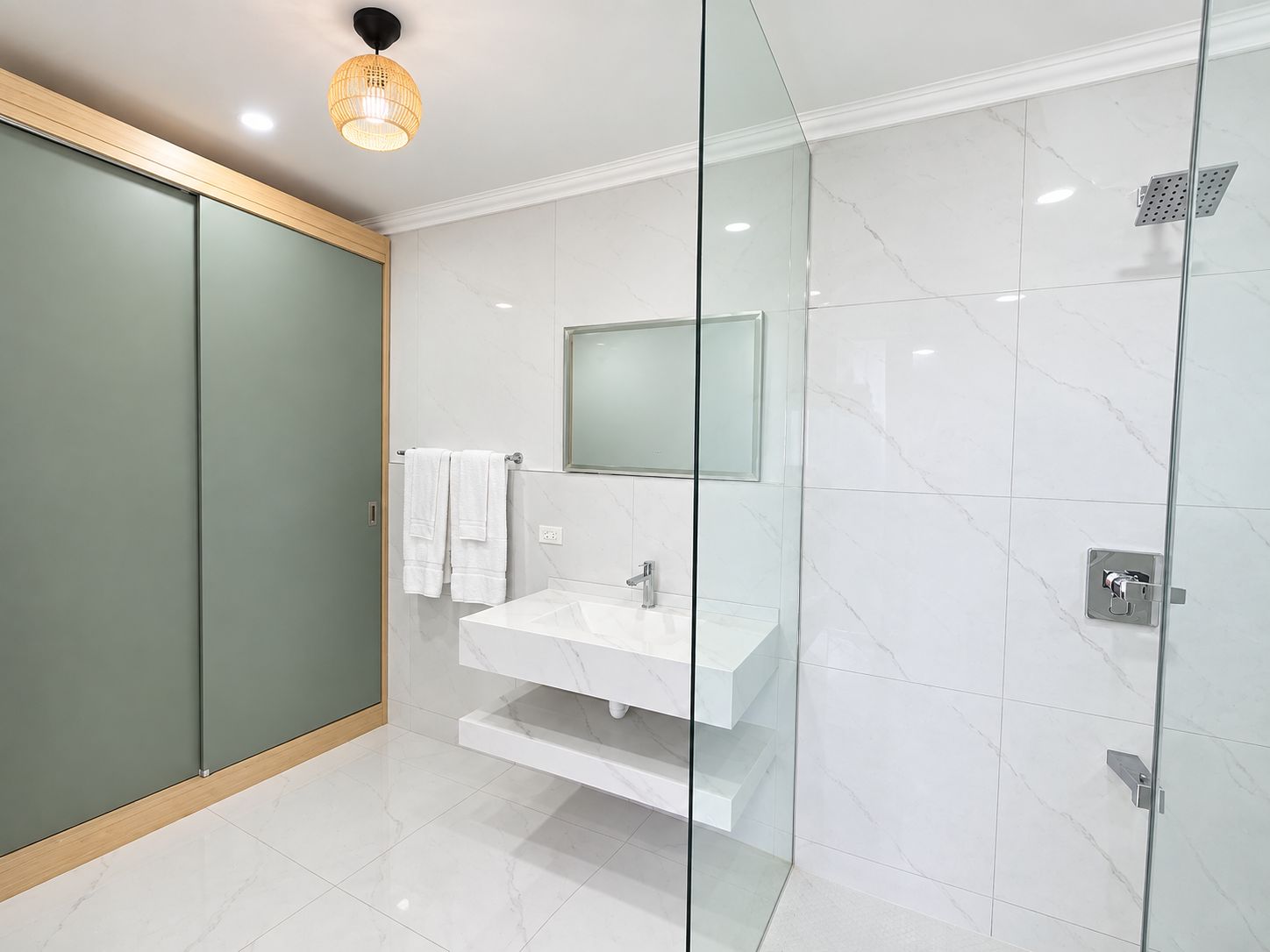 Une salle de bain moderne avec une douche à parois de verre, un lavabo blanc et un miroir au-dessus.