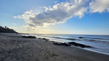 A beach with footprints in the sand, a rocky shoreline, and a clear sky with clouds.