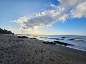 A beach with footprints in the sand, a rocky shoreline, and a clear sky with clouds.
