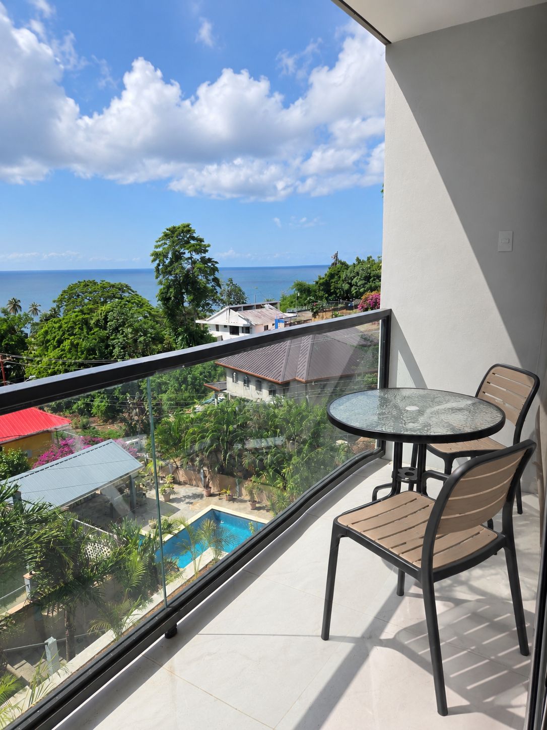 Ein Balkon mit Glasgeländer, der einen Pool und Meerblick bietet.