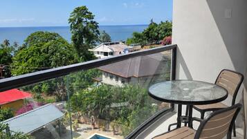 Ein Balkon mit Glasgeländer, der einen Pool und Meerblick bietet.