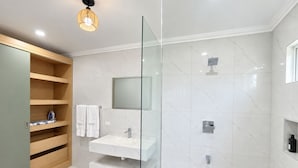 Un baño moderno con ducha envuelta en vidrio, tocador con espejo y estanterías integradas.