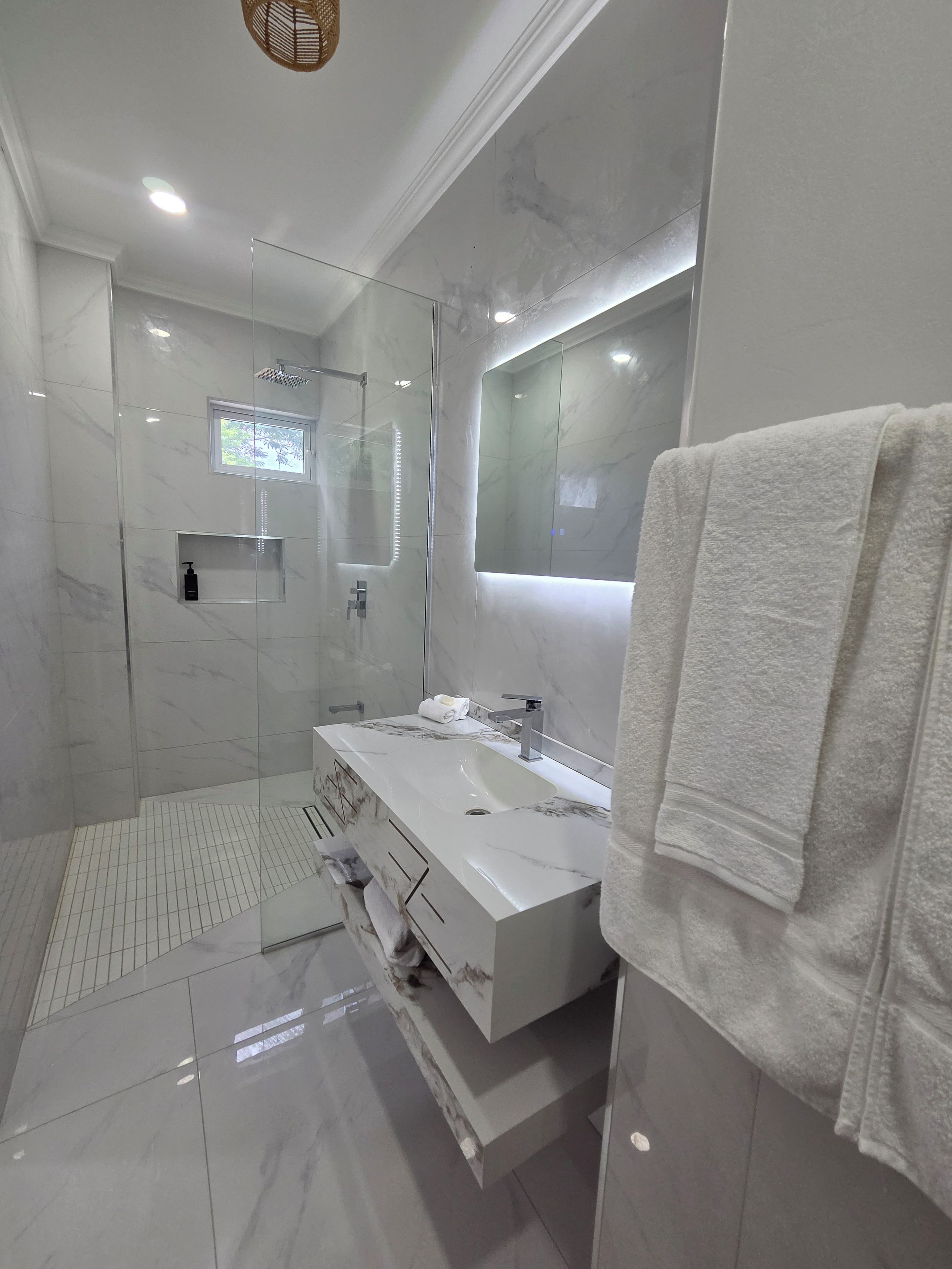 Un baño moderno con ducha envuelta en vidrio, un espejo grande y un tocador blanco con toallero.
