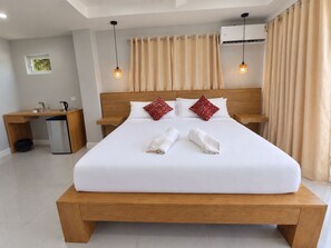 A hotel room with a large bed, bedside tables, a desk with a chair, a trash bin, and an air conditioning unit.