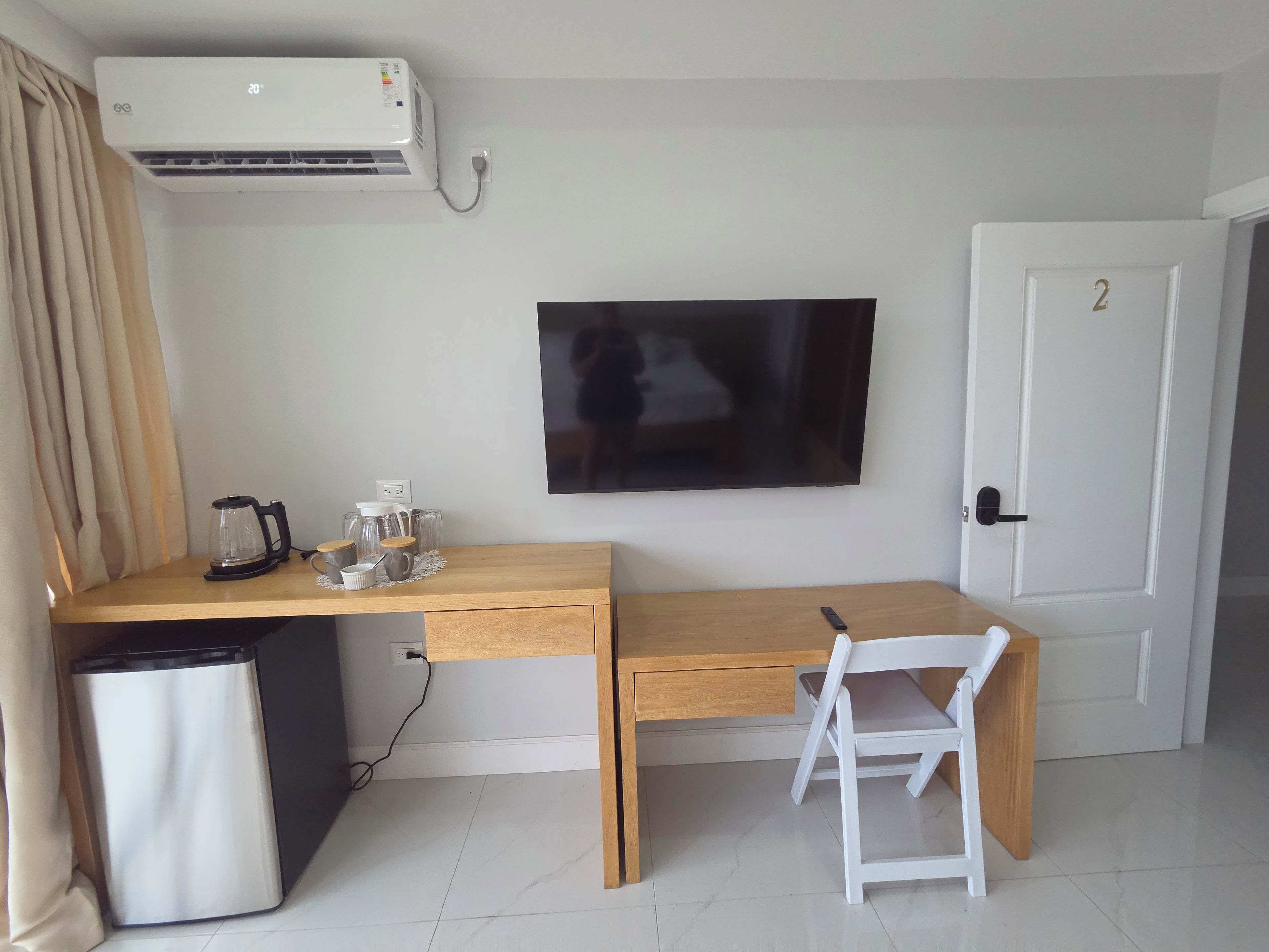 Ein kleines Zimmer mit Schreibtisch, Stuhl, Fernseher, Mülleimer und Klimaanlage.
