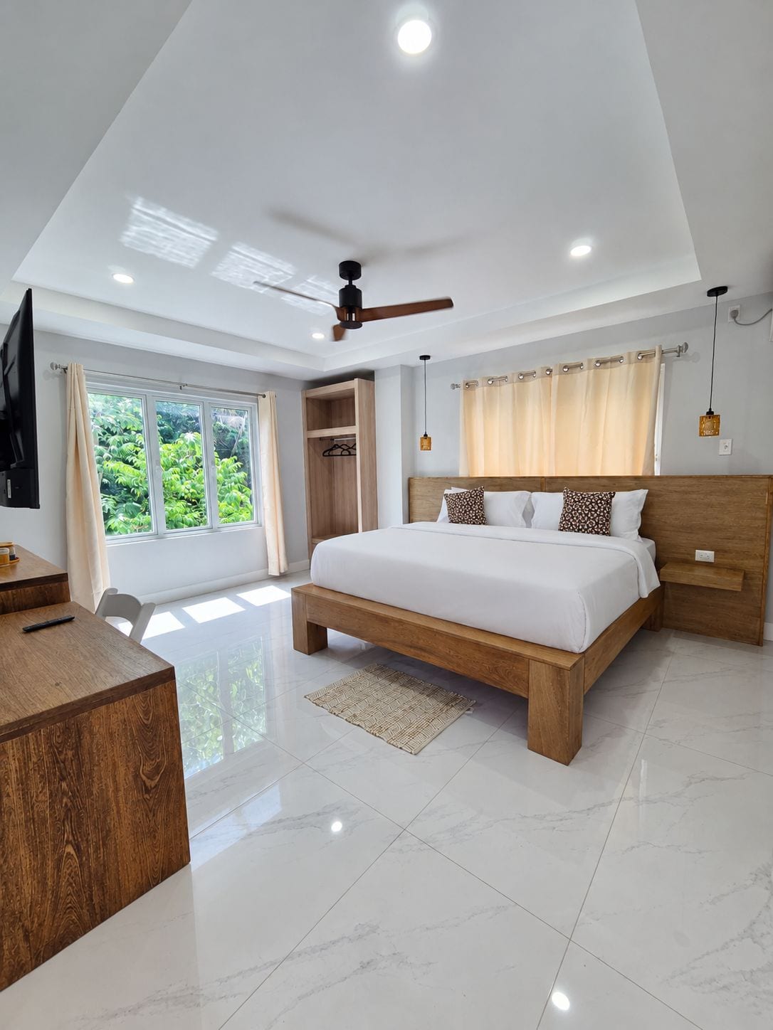 A modern bedroom with a large bed, a desk, and a ceiling fan.