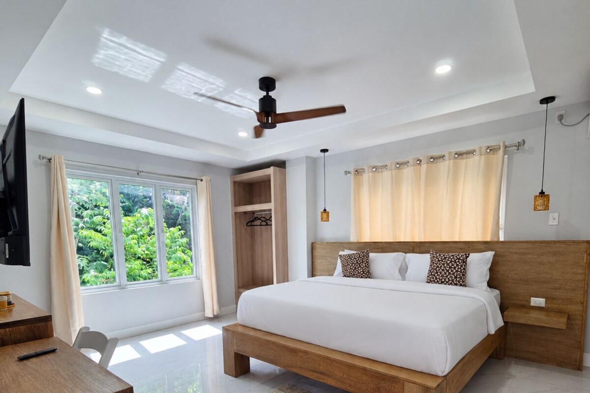 A modern bedroom with a large bed, a desk, and a ceiling fan.