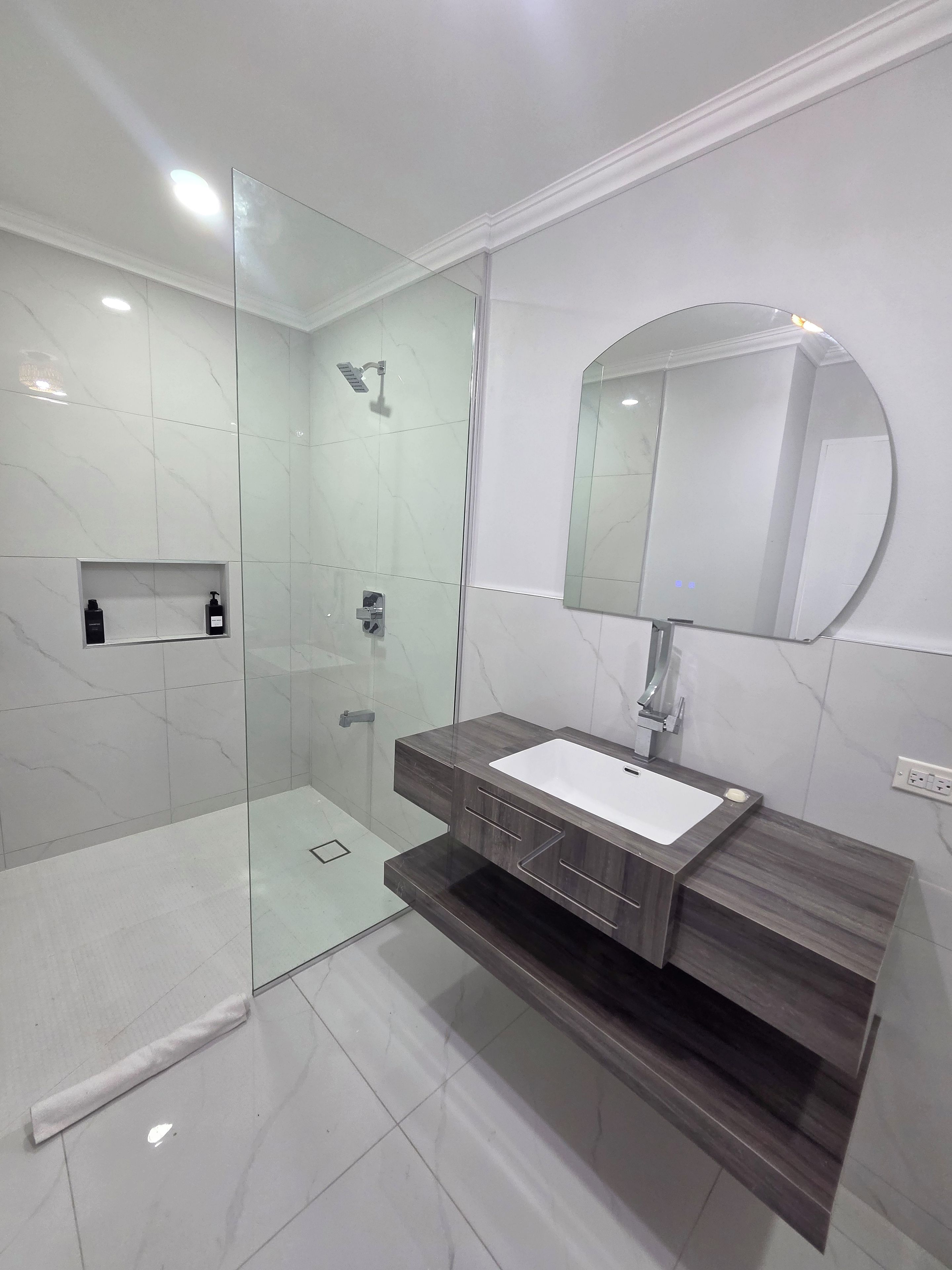 A modern bathroom with a glass-enclosed shower, a white sink, and a large mirror.