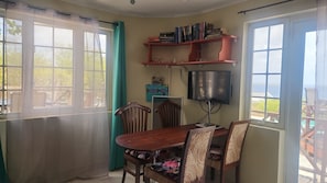 A dining area with a table and chairs, a bookshelf, a flat-screen TV, and a view of the outdoors.