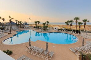 A swimming pool with lounge chairs and umbrellas, surrounded by palm trees and a view of the beach. - Captain Morgan`s Fort · New Listing! Steps to the Beach & Gulf Views (Gulf Shores)
