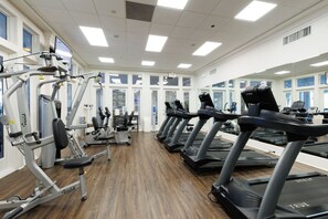 Une salle de sport équipée de plusieurs tapis de course, de machines de musculation et dotée d’un plancher en bois.