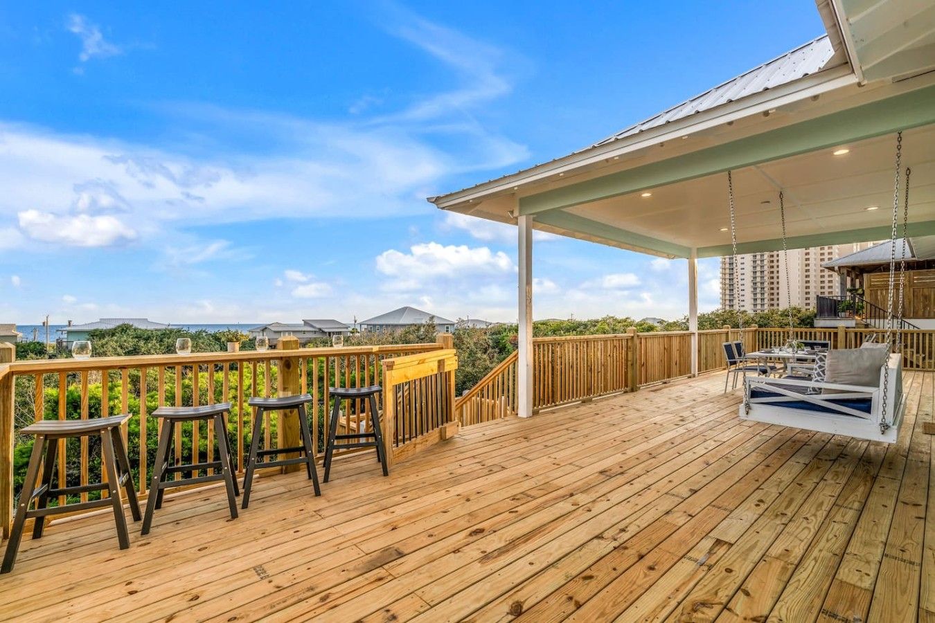 A wooden deck with outdoor seating, a swing, and a covered area with a view of the ocean and buildings.