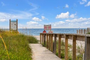 Een houten looppad dat naar een strand leidt, met een redderpost en een informatiebord.